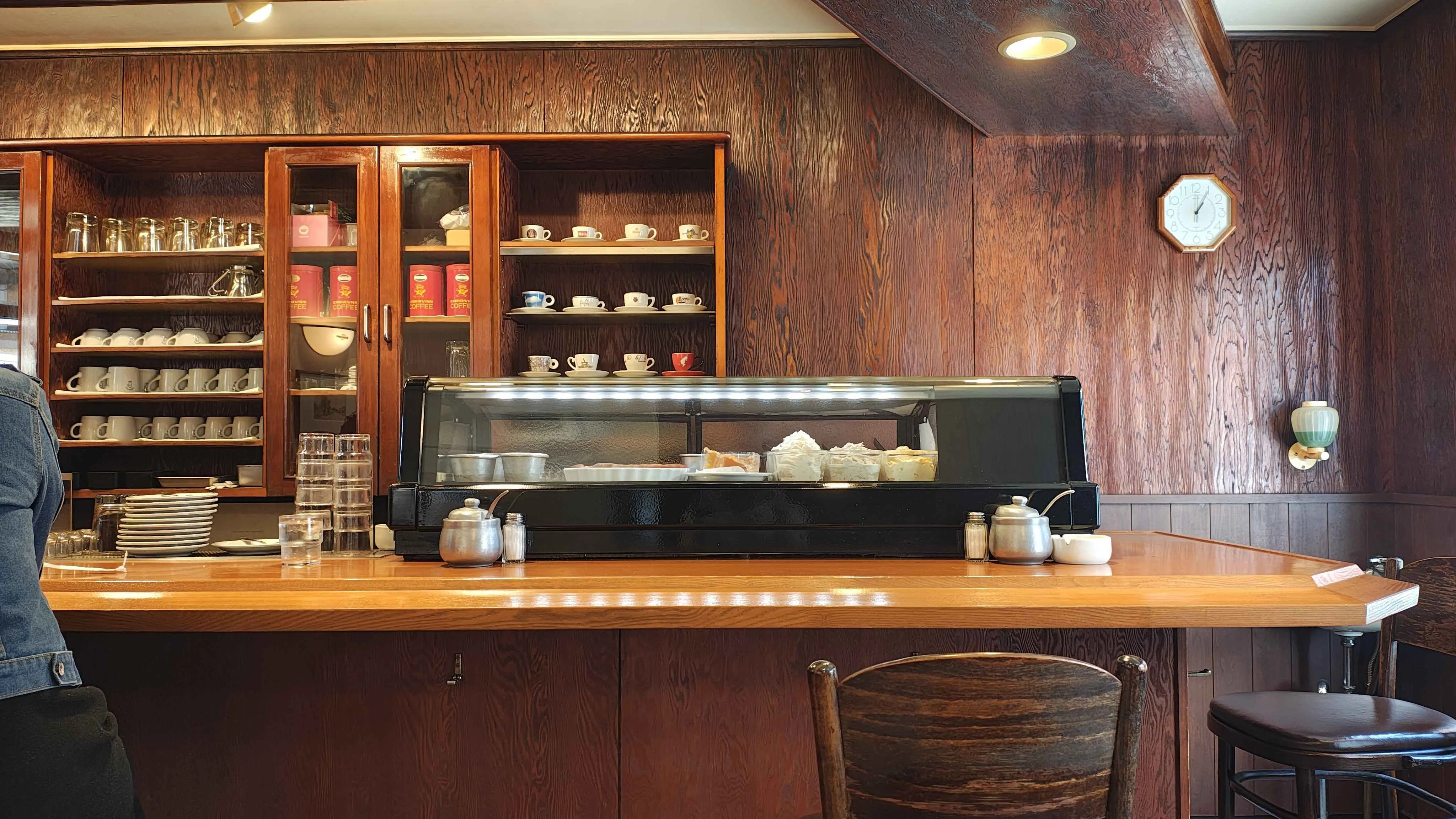 木のカウンターと、カップの並ぶ棚が見える cafe RONDINO の店内